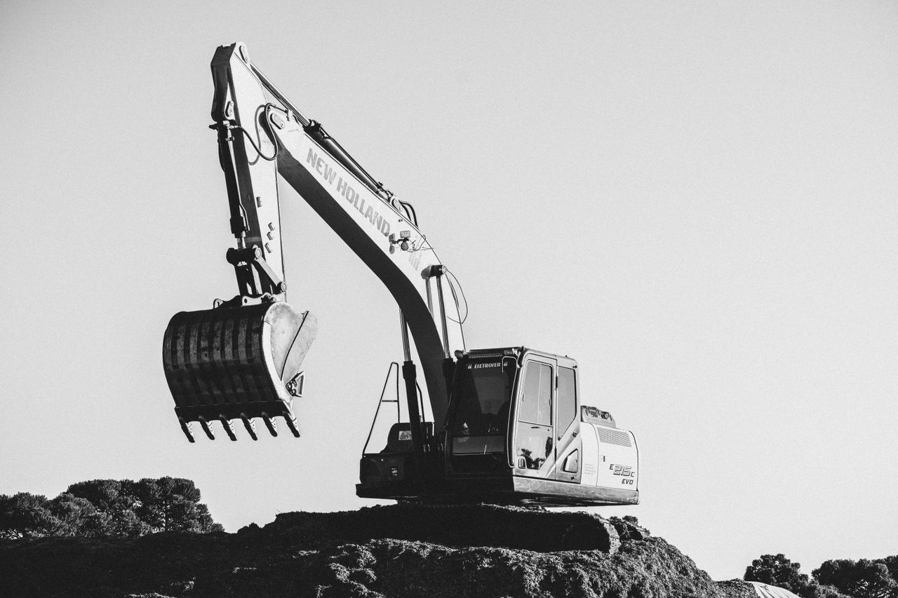 Black and white image of an excavator at a construction site under a clear sky.