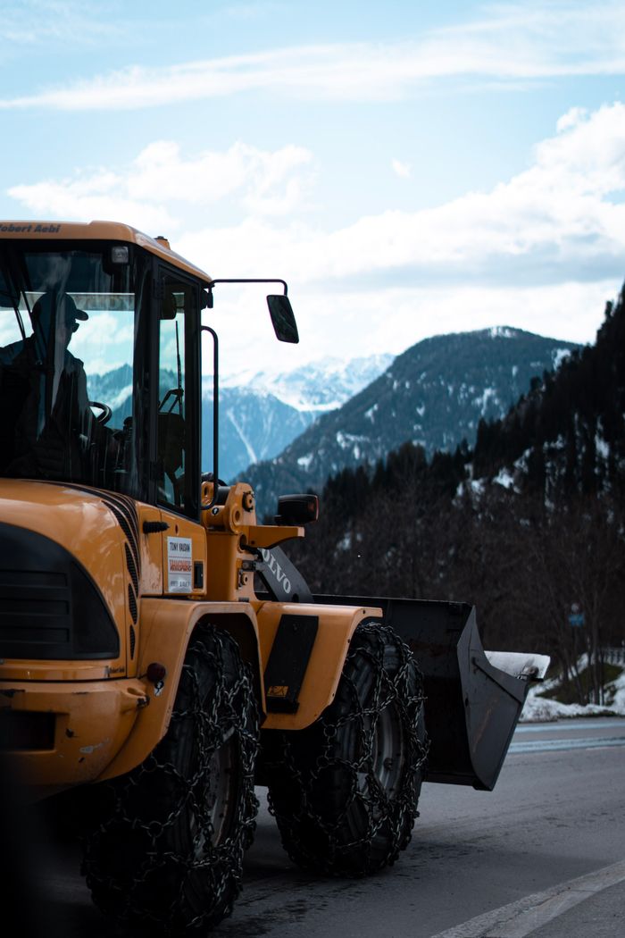 Yellow snowplow on a mountain road in a snowy winter landscape with snowy peaks.