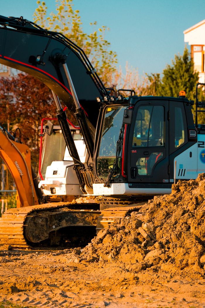 Excavator at a construction site with dirt piles and trees in background.