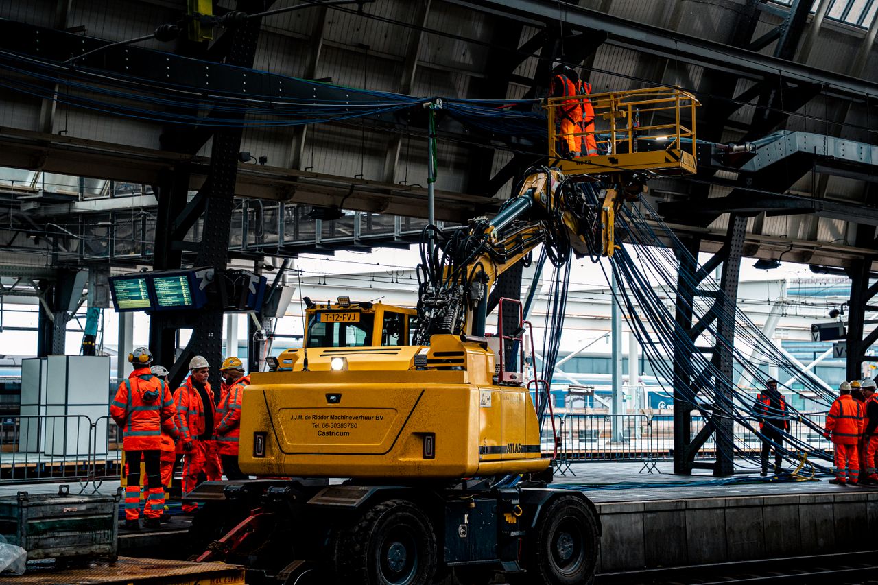 Workers in high-visibility clothing operate machinery at a train station, ensuring safety and efficiency.