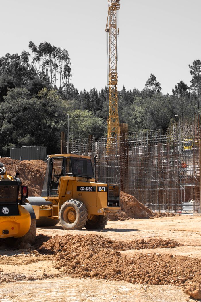 A construction site featuring a bulldozer and crane against a wooded backdrop.