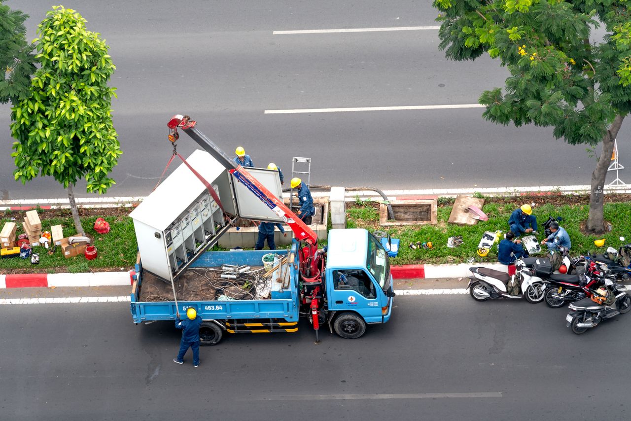 Utility workers using a crane truck for maintenance on a city street, viewed from above.
