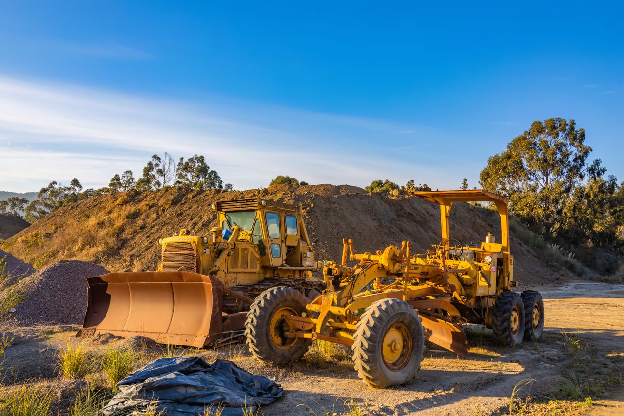 Yellow bulldozer and grader on a dirt construction site under blue sky.