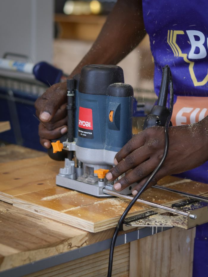 Close-up of hands operating a router on wood in a workshop, highlighting craftsmanship.
