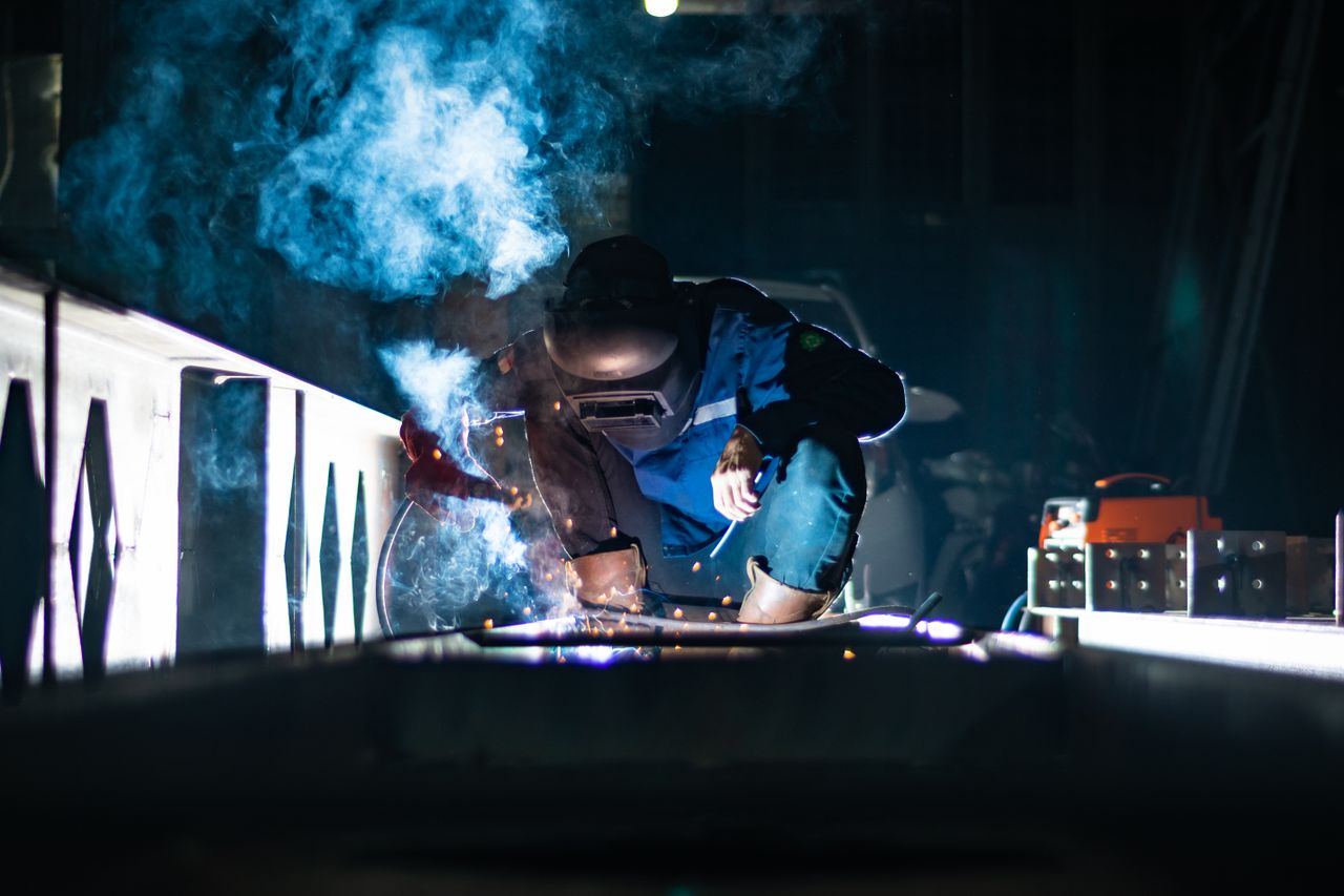 A welder working at night producing sparks and smoke in an industrial setting.