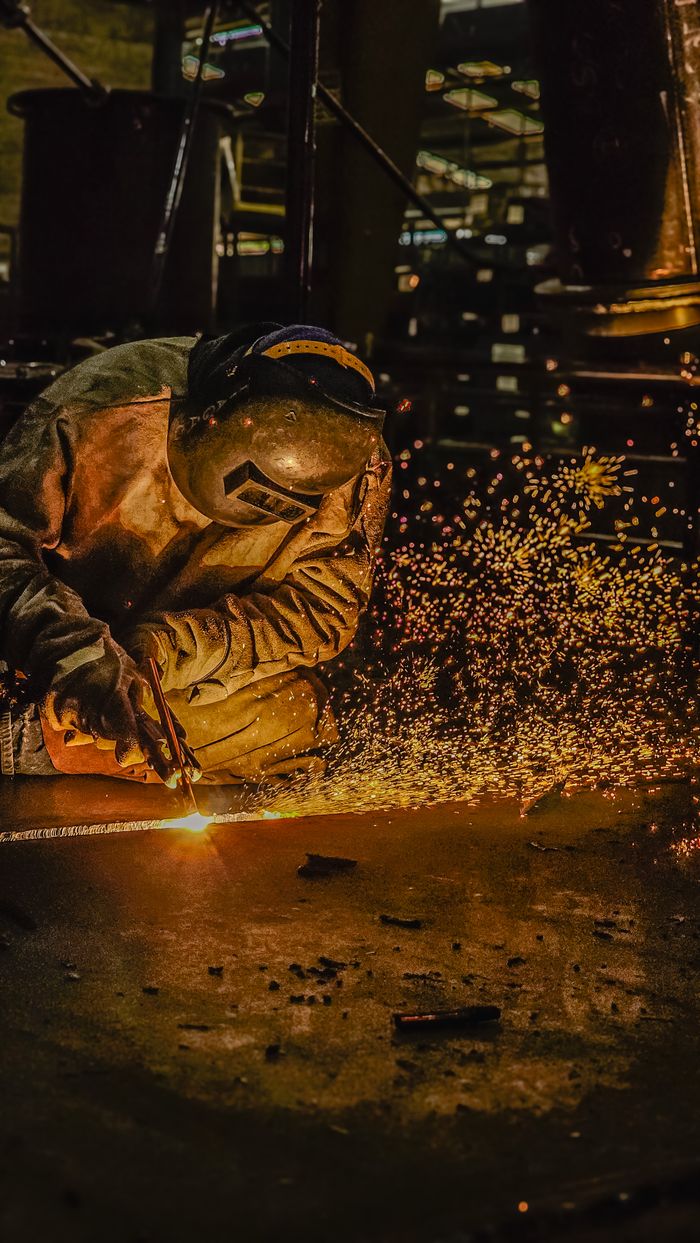 A welder in protective gear works with sparks flying in an industrial setting.