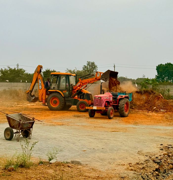 Excavator and tractor working together on a construction site in Attibele, India.
