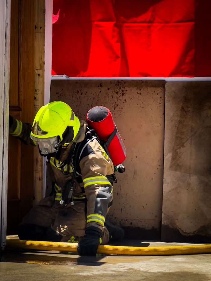 A firefighter in full gear kneels during an emergency response with a hose, showing bravery and dedication.