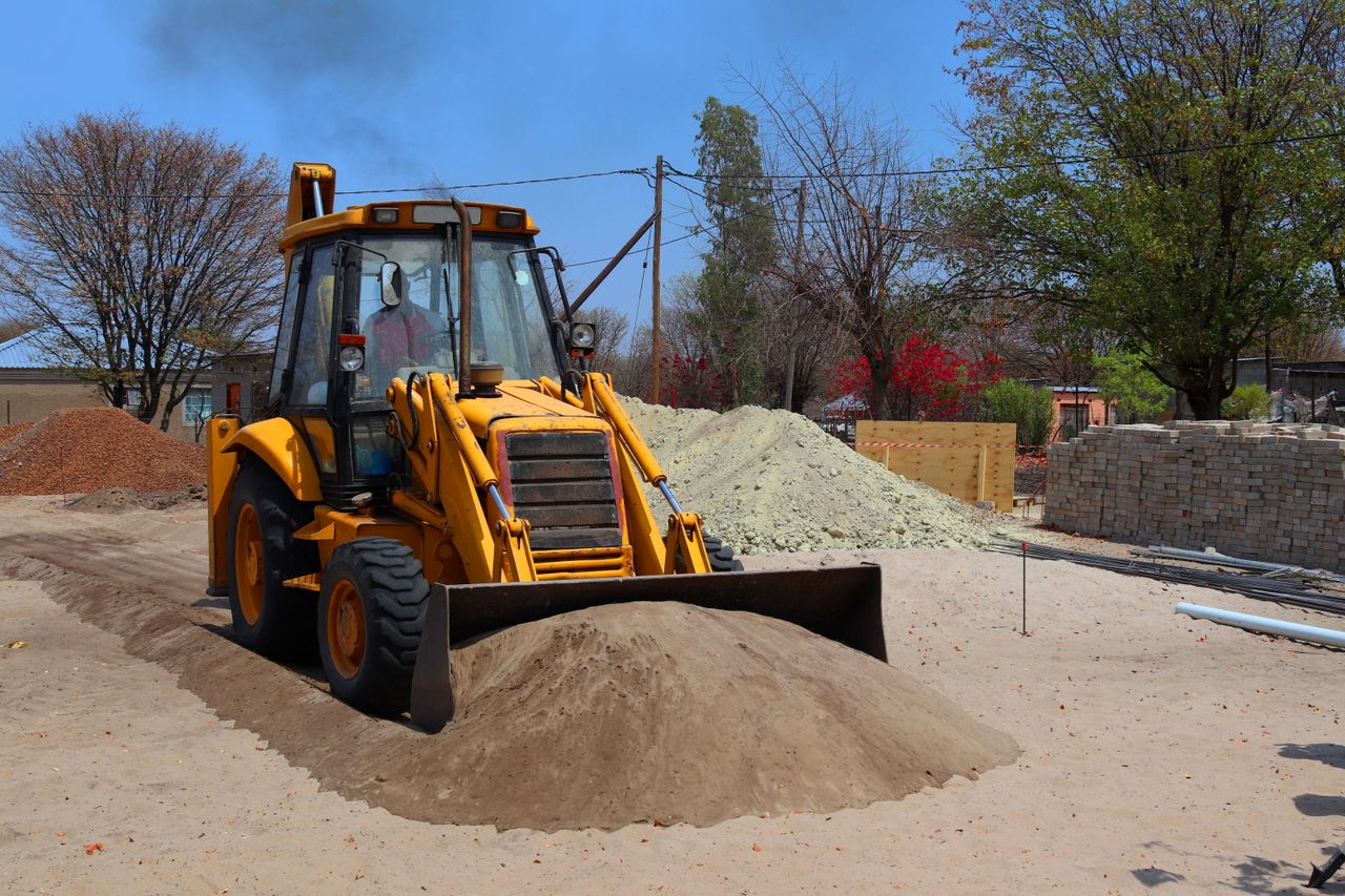 A yellow backhoe loader at a construction site moving sand on a clear day.